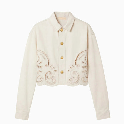 A cream-colored, long-sleeve button-up jacket from Ulla Johnson, The Bobbi Eyelet Jacket, featuring gold buttons and intricate eyelet embroidery cut-out patterns along the lower front and hem.