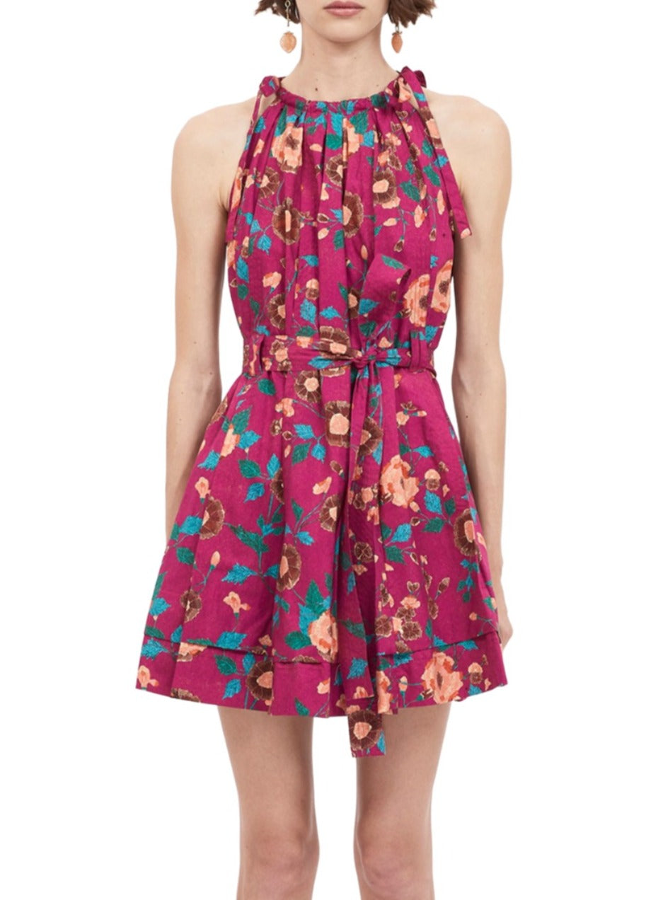 The Ulla Johnson Brienne Dress is a sleeveless, knee-length garment crafted from poplin, featuring a high neckline and floral pattern in shades of pink, red, and teal. It's cinched at the waist with a matching tie belt for an effortlessly chic look.