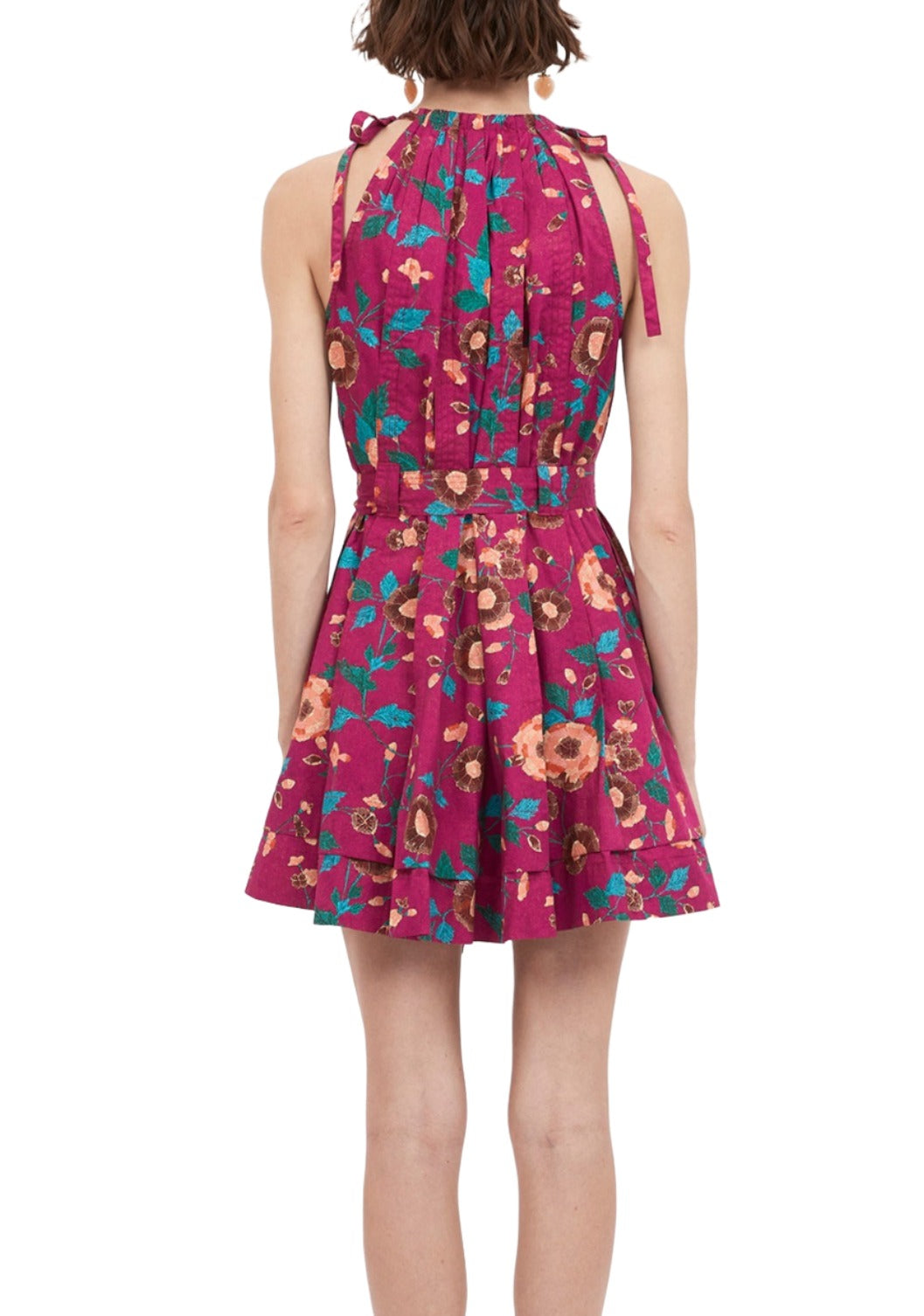 Person wearing a sleeveless, bright pink Ulla Johnson Brienne Dress with a floral pattern, seen from the back. The dress, made of poplin, has tie straps at the shoulders and a flared skirt.