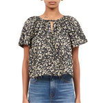 A person wearing the Ulla Johnson Sena Top, a black and white floral vines short-sleeve blouse from Ulla Johnson, paired with blue jeans.