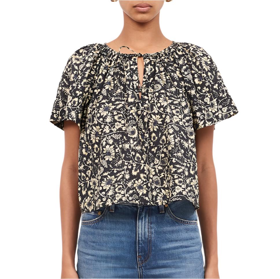 A person wearing the Ulla Johnson Sena Top, a black and white floral vines short-sleeve blouse from Ulla Johnson, paired with blue jeans.