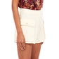 A person is wearing Ulla Johnson Sadie Shorts in beige cotton tencel with side pockets, paired with a floral top, photographed from the waist down.