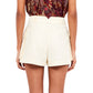 A person wearing a patterned, sleeveless top and Ulla Johnson's Sadie Short, made of cream-colored cotton tencel with pockets, stands with their back to the camera.