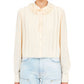 A person is wearing the Ulla Johnson Karla Blouse, a luxurious silk button-up in light cream with a frilled collar, paired perfectly with light blue jeans.