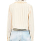 Someone wearing the Karla Blouse by Ulla Johnson, a cream pleated silk top, paired with light blue jeans, is seen from the back against a plain background.