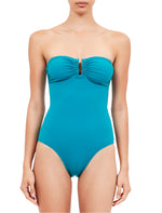 A woman models the Ulla Johnson Monterey Maillot One Piece, a strapless swimsuit with a sweetheart neckline, ruched front, keyhole detail, and full coverage bottom, set against a white background.