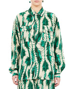 A person wearing Ulla Johnson's Soren Shirt, a green and beige patterned design with matching pants, crafted from 100% silk, stands with arms relaxed.