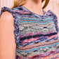 A woman stands in front of a light, textured background wearing the Ulla Johnson Ajak Knit Dress, a sleeveless, rib-knitted piece featuring multicolored stripes and ruffled shoulder trim.
