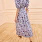 A person wearing the Ulla Johnson Adriana Dress in blue and white cotton poplin with puff sleeves and brown heeled sandals stands in a beige carpeted room.