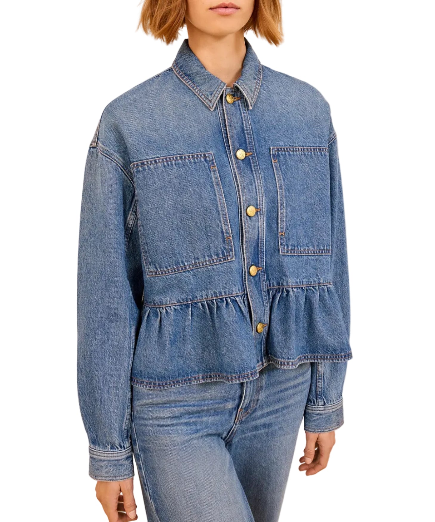 A person wearing Ulla Johnson's blue denim Arquette Jacket, featuring large front pockets, gold buttons, and a ruffled hem, paired with relaxed fit blue jeans.