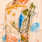A woman wears the Ulla Johnson Artist Blouse, a collared long-sleeve top in satin-faced poplin with an abstract multicolored print featuring orange, blue, green, and beige tones.