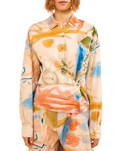 A person wearing the Ulla Johnson Artist Blouse and matching pants, both featuring an abstract, multicolored watercolor pattern in orange, blue, green, and yellow.