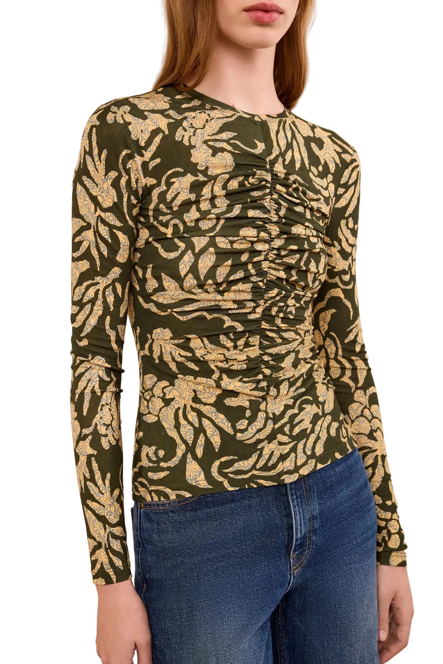 A woman wears the Ulla Johnson Asha Jersey Top, a ruched long-sleeve crewneck featuring a green and yellow leaf pattern, paired with blue jeans.