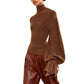 A person wearing the Ulla Johnson Camille Knit Pullover with elongated sleeves and brown pants, standing against a white background.