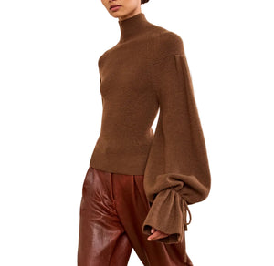 A person wearing the Ulla Johnson Camille Knit Pullover with elongated sleeves and brown pants, standing against a white background.