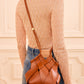 A woman in a sheer pink lace top and blue jeans is shown from the back, wearing the Ulla Johnson Charlotte Crossbody bag.