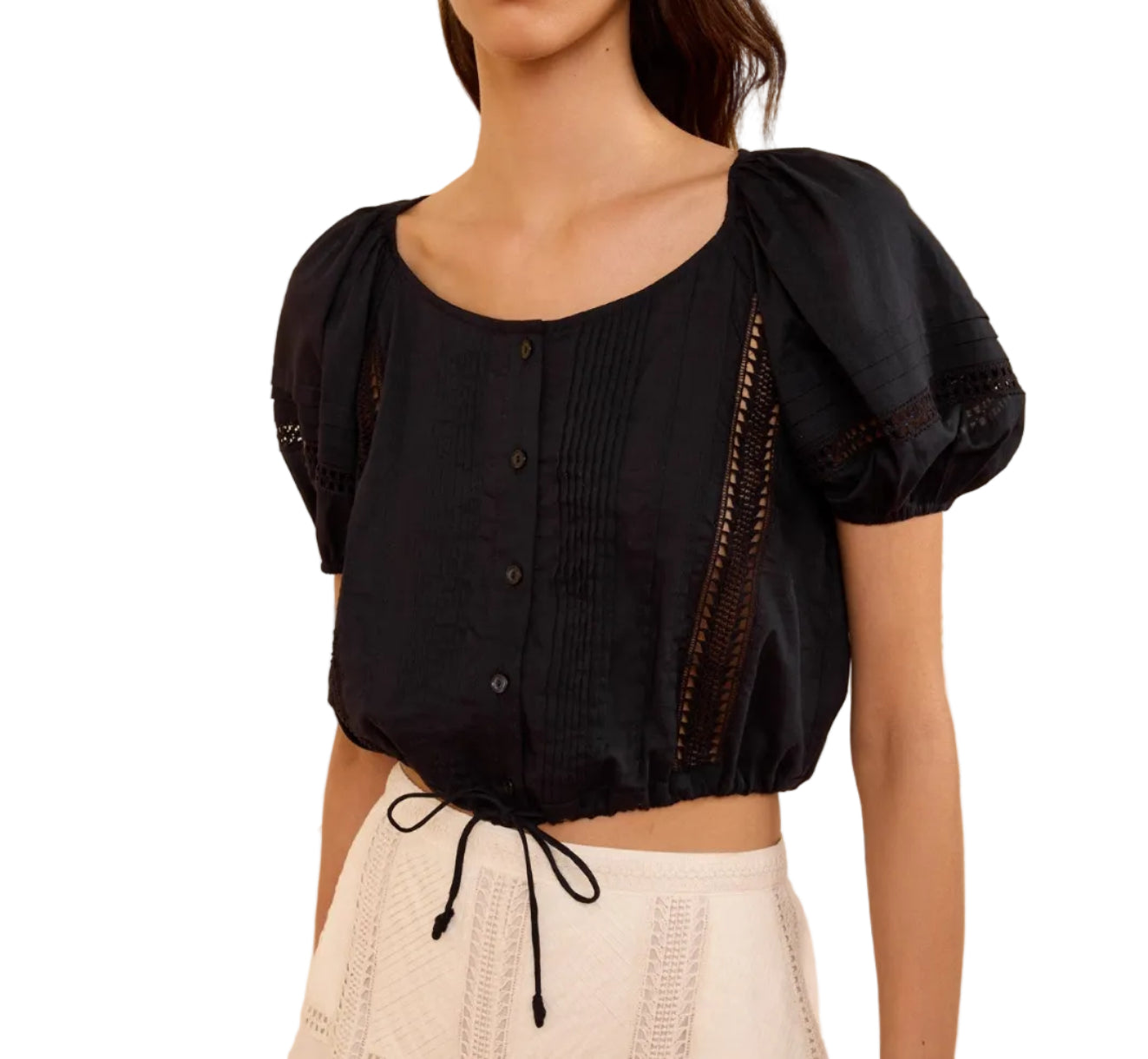A woman wears the Ulla Johnson Clara Top—a cropped black cotton blouse featuring short sleeves, button-front closure, and delicate lace details reminiscent of a Victorian lace top—paired with high-waisted cream shorts.