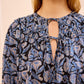 A woman wearing the Ulla Johnson Florelle Blouse, featuring blue and beige ikat-inspired florals on shadow-striped cotton and a keyhole neckline with a string tie.