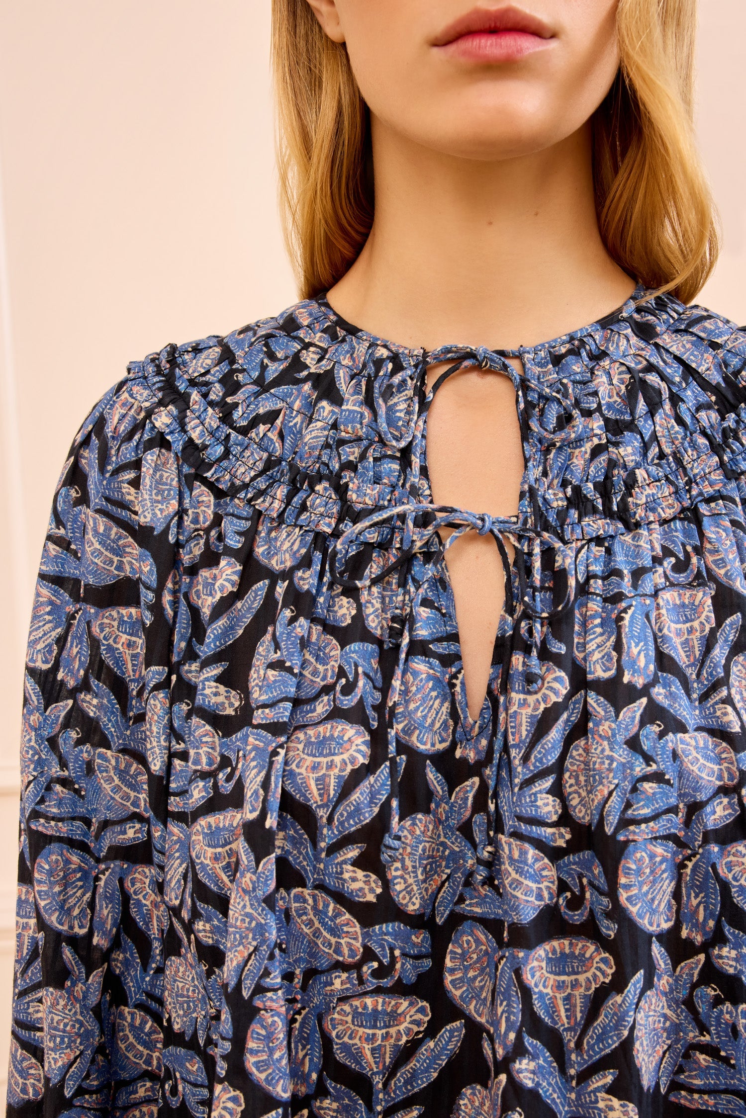 A woman wearing the Ulla Johnson Florelle Blouse, featuring blue and beige ikat-inspired florals on shadow-striped cotton and a keyhole neckline with a string tie.