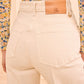 Person wears the Ulla Johnson Genevieve Stretch Jean—high-waisted, wide-leg white denim with a tan leather waistband patch—paired with a floral long-sleeve top.