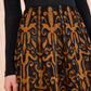 A person wearing a black long-sleeve top and the Ulla Johnson Gili Midi Skirt, which features intricate black and brown Victorian-inspired embroidery.