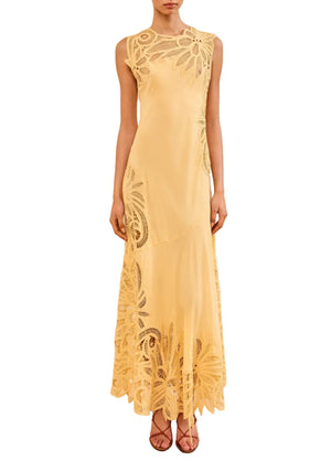 A person wears the Ulla Johnson Idra Applique Dress, a dandelion yellow silk piece with a body-skimming fit and lace floral cutouts, paired with strappy sandals against a plain background.