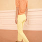 A person stands indoors wearing the Ulla Johnson Jude Embellished Top, yellow pants, and olive green heeled shoes, facing slightly away from the camera.