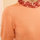 Model wears the Ulla Johnson Jude Embellished Top in peach with short sleeves, paired with a chunky pink sequin necklace, shown from shoulders to mouth against a neutral background.