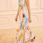 A woman wearing the sleeveless Lana Ruched Jersey Dress by Ulla Johnson, inspired by Helen Frankenthaler’s colorful abstract art, walks indoors on a patterned carpet.