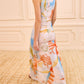 A woman in a sleeveless Ulla Johnson Lana Ruched Jersey Dress, inspired by colorful abstract art, walks on a beige carpet in a room with cream paneled walls.