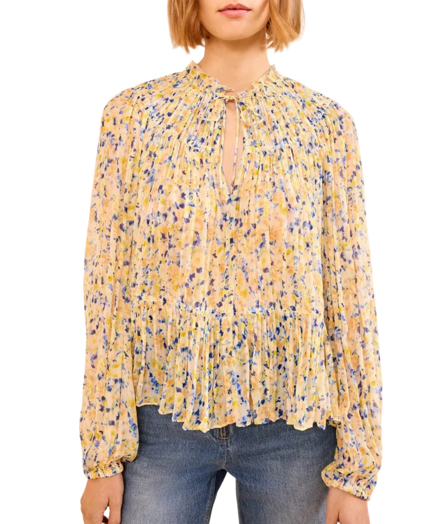 A woman wears the Leandra Silk Blouse by Ulla Johnson—a long-sleeve, yellow floral silk blouse with pleats and a keyhole neckline—paired with blue jeans.