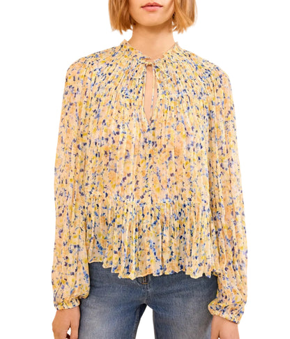 A woman wears the Leandra Silk Blouse by Ulla Johnson—a long-sleeve, yellow floral silk blouse with pleats and a keyhole neckline—paired with blue jeans.