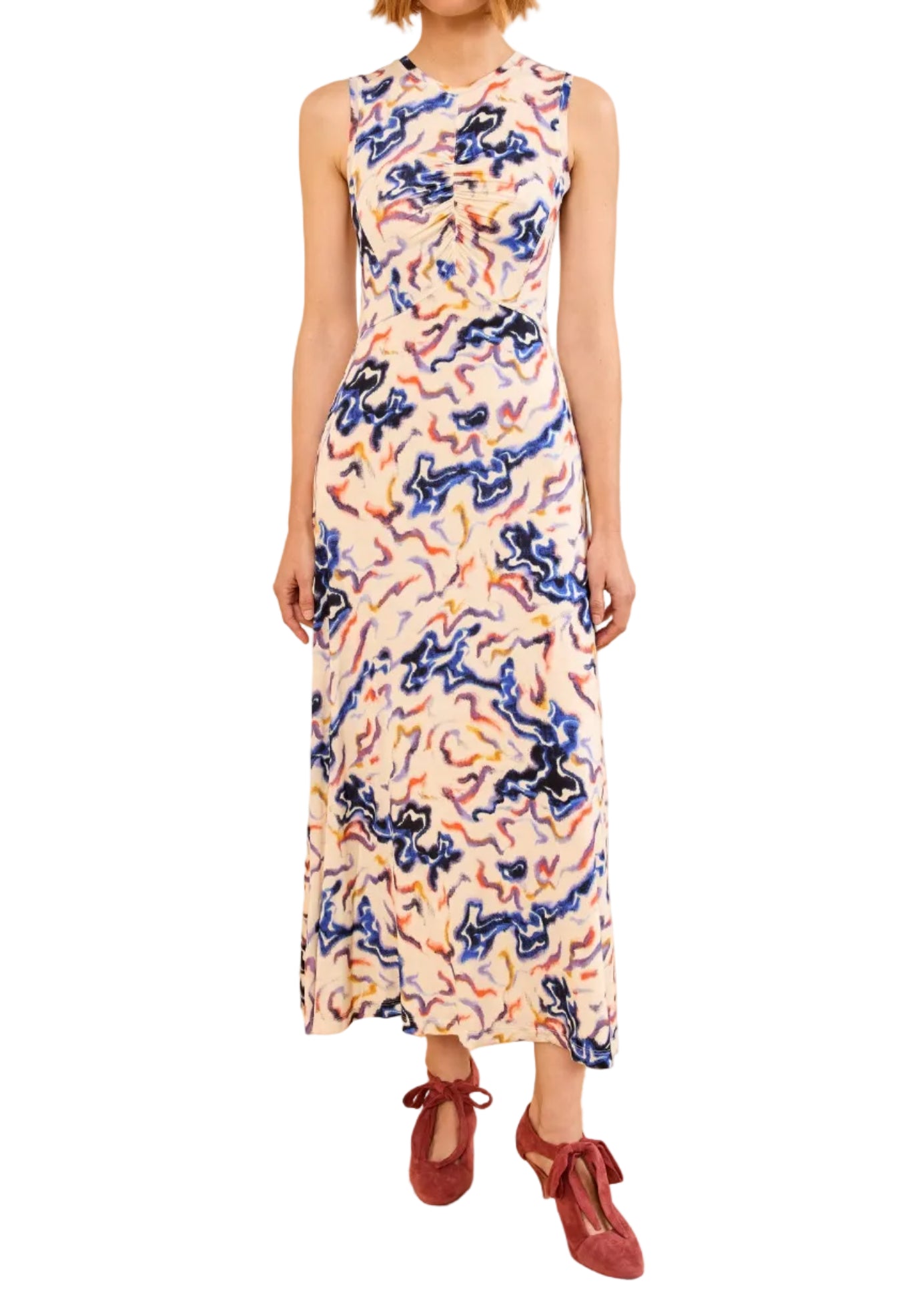 A woman in the Ulla Johnson Lina Jersey Dress, a sleeveless, ankle-length dress with a vibrant vintage ikat print, and red flat shoes stands against a white background.