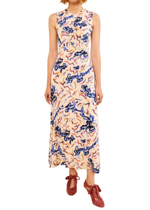 A woman in the Ulla Johnson Lina Jersey Dress, a sleeveless, ankle-length dress with a vibrant vintage ikat print, and red flat shoes stands against a white background.