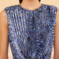 A woman wears the Ulla Johnson Malin Satin Dress, a sleeveless, pleated midi with a blue and black abstract pattern, shown from shoulders to waist.