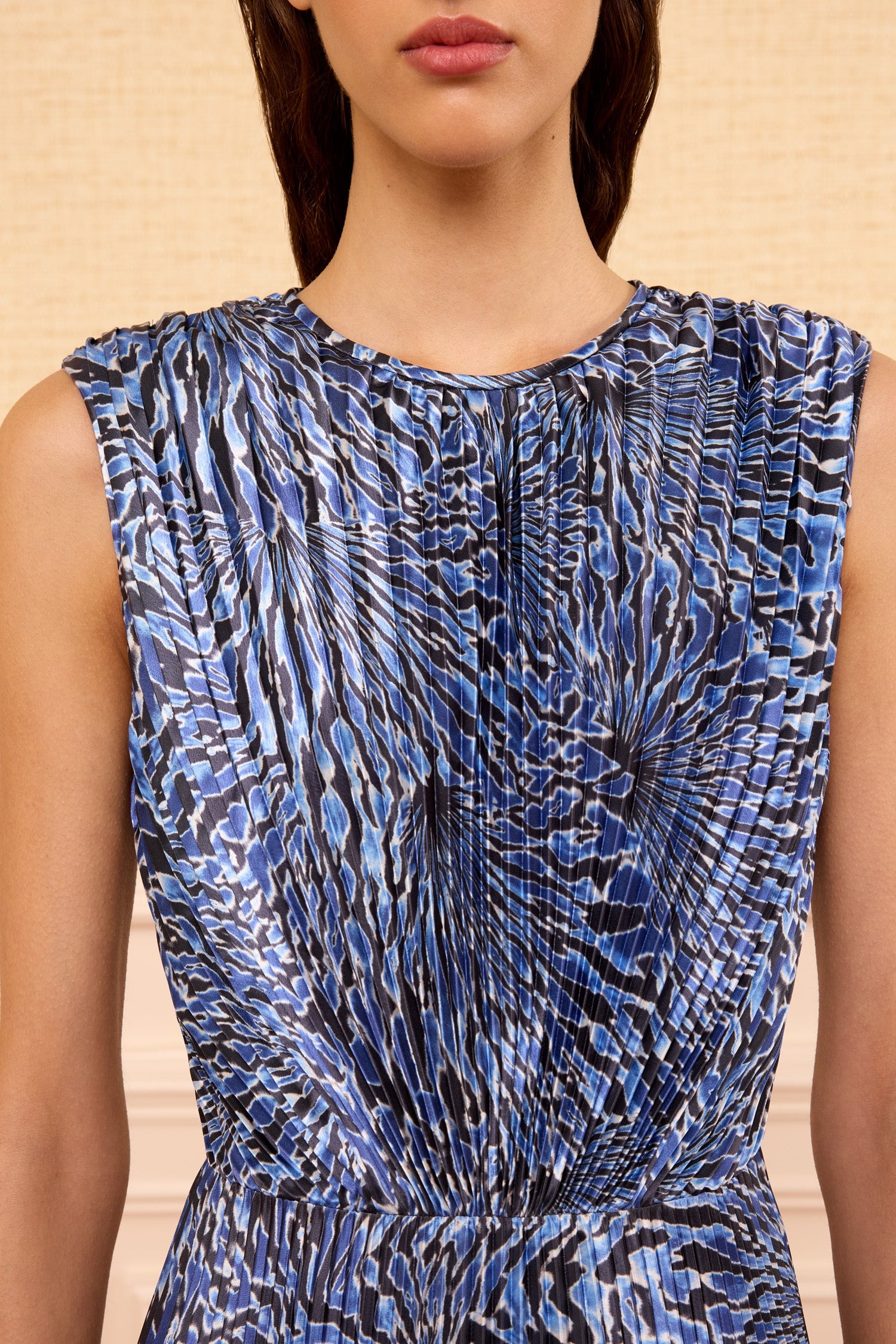 A woman wears the Ulla Johnson Malin Satin Dress, a sleeveless, pleated midi with a blue and black abstract pattern, shown from shoulders to waist.