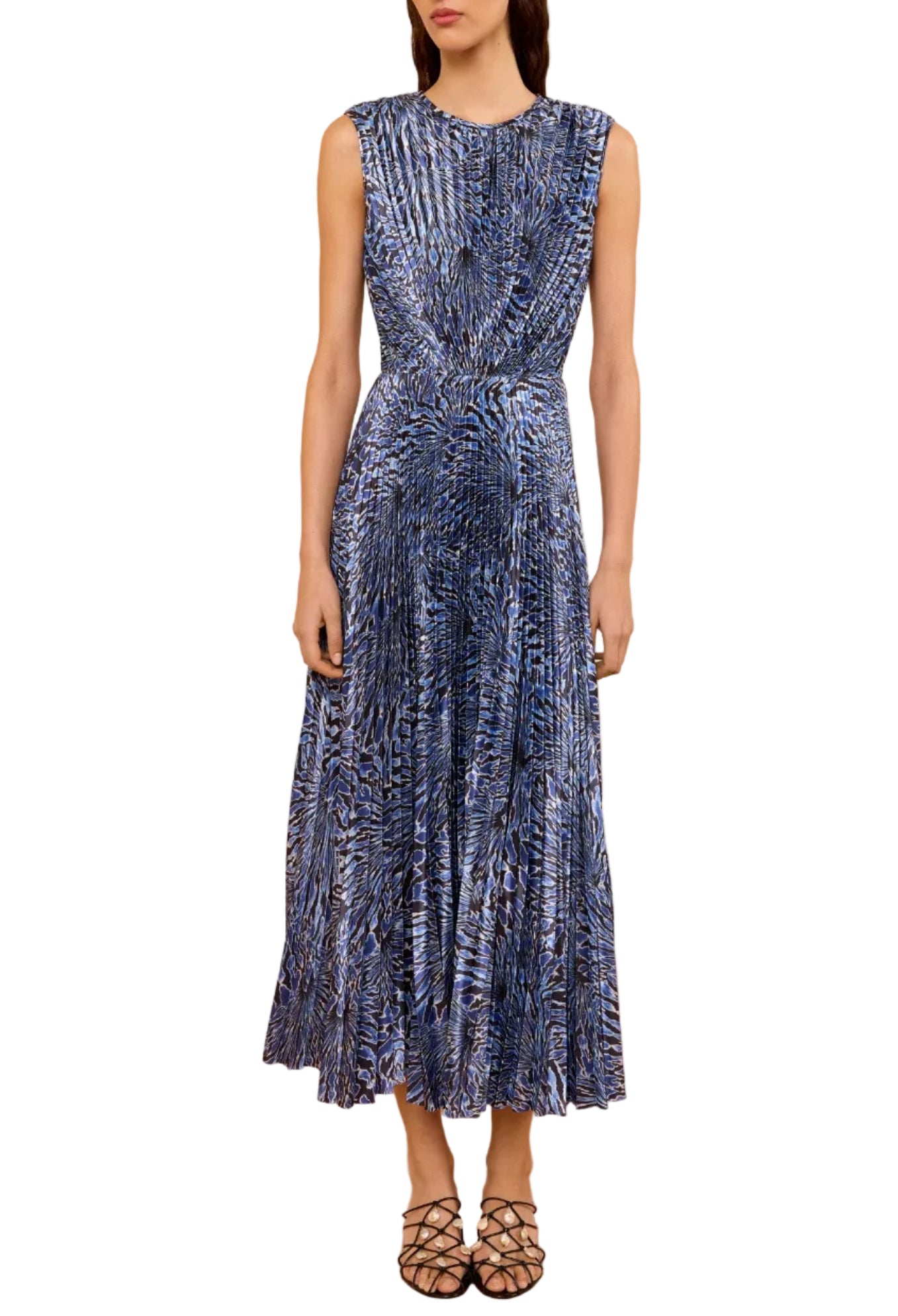 A woman in the Ulla Johnson Malin Satin Dress—a sleeveless, ankle-length blue and black patterned pleated midi—stands against a white background wearing black strappy shoes.