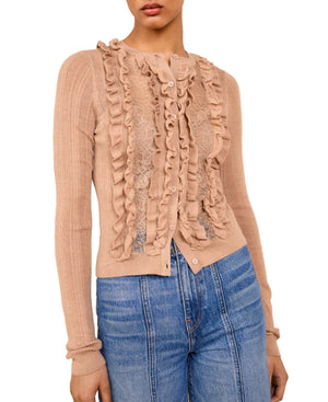A woman wears the Ulla Johnson Maryel Cardigan, a light brown long-sleeve merino wool piece with ruffle and lace details on the front, paired with high-waisted blue jeans.