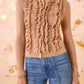 A person wearing the Ulla Johnson Maryel Cardigan, a beige, long-sleeve merino wool piece with ruffle and lace details, paired with blue high-waisted jeans.