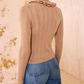A person wearing the Ulla Johnson Maryel Cardigan, a ribbed merino wool sweater with long sleeves and a ruffled collar, paired with blue jeans, seen from the back.