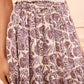 A person wearing a light ribbed top and the Ulla Johnson Nessa Skirt, a flowy cotton-blend piece with purple and white batik-inspired florals and an elastic waist.