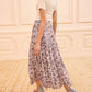 A woman walks indoors on a carpeted floor, wearing a short-sleeve white ribbed top, light blue block-heeled sandals, and the Nessa Skirt by Ulla Johnson—a flowy cotton-blend skirt with batik-inspired florals and an elastic waist.