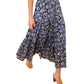 A person wearing the Nessa Skirt by Ulla Johnson—a batik-inspired floral cotton-blend maxi with an elastic waist—and tan sandals stands on a beige carpet with a geometric design.
