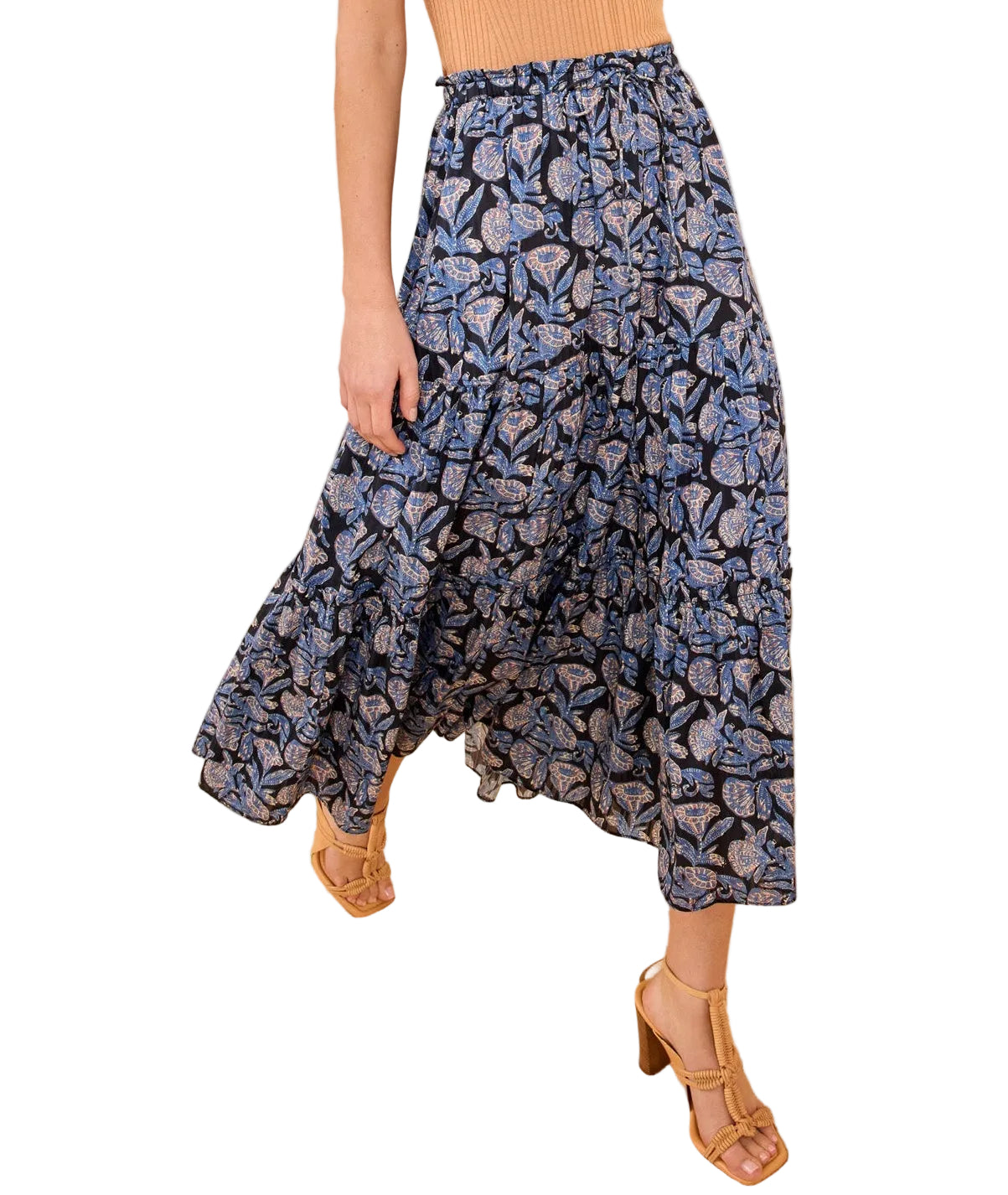 A person wearing the Nessa Skirt by Ulla Johnson—a batik-inspired floral cotton-blend maxi with an elastic waist—and tan sandals stands on a beige carpet with a geometric design.