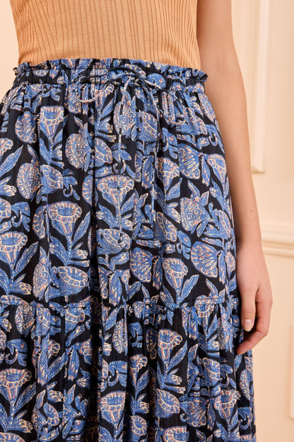 A person wears a sleeveless, ribbed tan top paired with the Ulla Johnson Nessa Skirt—a high-waisted, cotton-blend piece featuring batik-inspired florals.