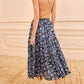 A woman, seen from behind on a beige checkered carpet, wears a tan sleeveless top, tan heeled sandals, and the Ulla Johnson Nessa Skirt—a blue cotton-blend skirt with batik-style florals and an elastic waist.