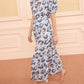 A woman wearing the Ulla Johnson Olina Midi Skirt, featuring a light blue and navy pattern, walks in strappy sandals on a carpeted floor.