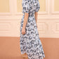 A woman stands indoors wearing the Ulla Johnson Olina Midi Skirt, featuring a light blue and white floral cotton-blend pattern, styled as a dress with beige heeled sandals.