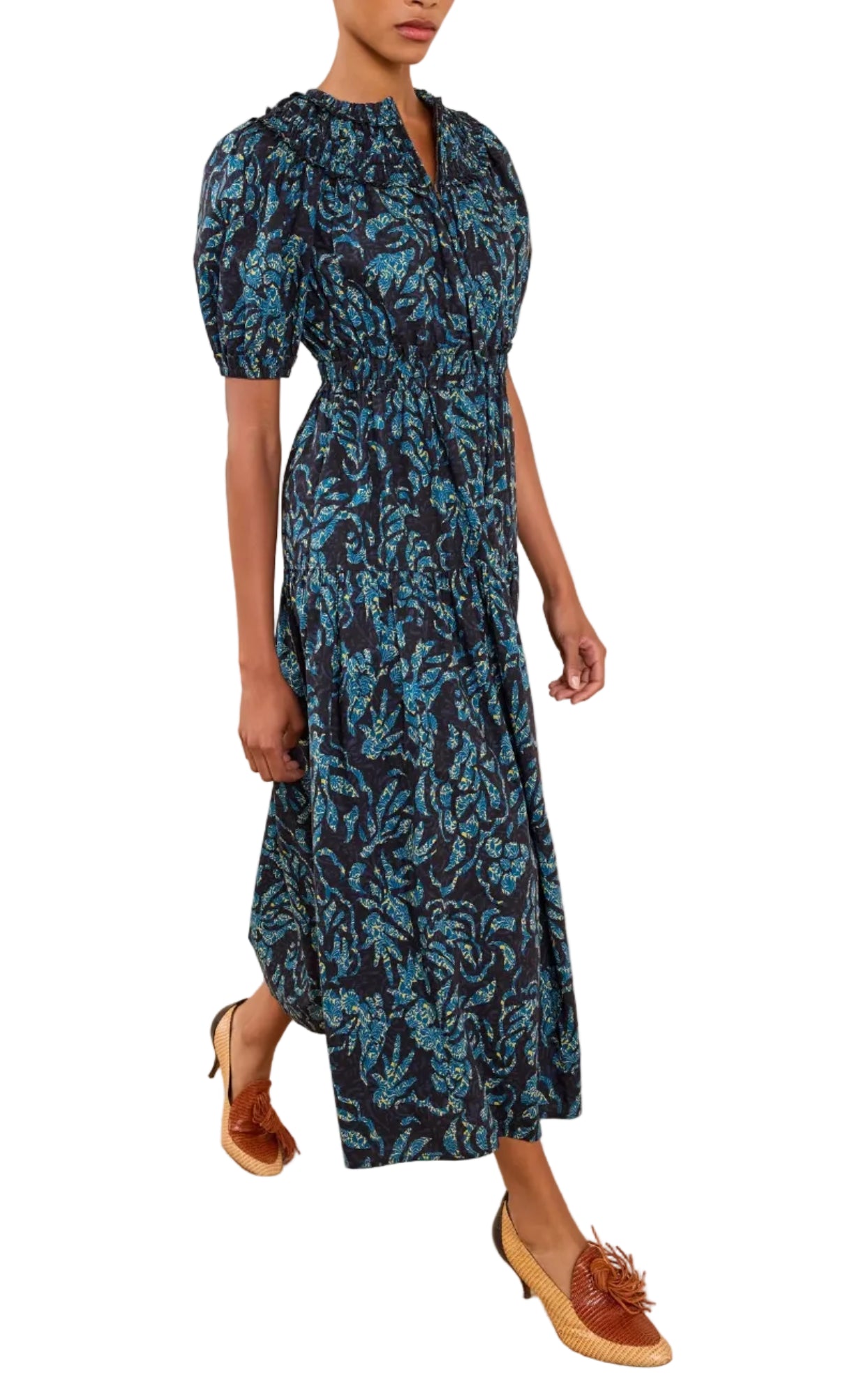 A person wearing the Ulla Johnson Othella Cotton Dress in dark blue with a mid-length floral design and short sleeves, paired with brown heeled loafers, walks forward.