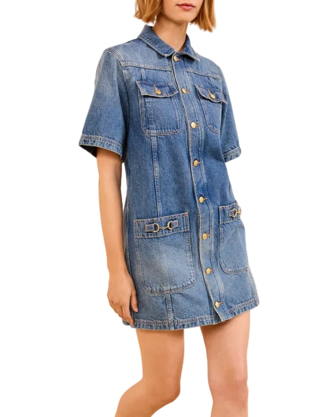 A person wears the Ulla Johnson Painters Dress, a short-sleeve denim dress with a shirt-inspired silhouette and front pockets, paired with tan heeled shoes tied with bows.